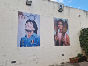 Wandbilder in Bacoli bei Neapel: Diego Maradona, der den SSC Napoli zu seinen größten Erfolgen führte und bis heute in der ganzen Region fast schon wie ein Heiliger verehrt wird. Daneben ein Motiv mit Sophia Loren, die im nahen Pozzuoli aufwuchs. (Foto: © Bastian Glumm)