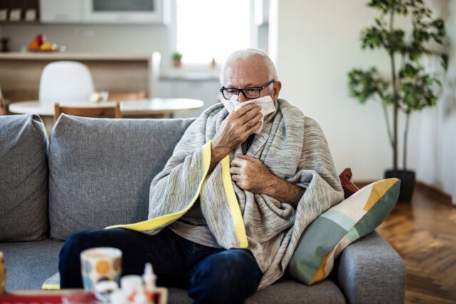 Shot of a sickly senior man blowing his nose with a tissue at home. Fieber, Husten und Erschöpfung: Die aktuelle Grippewelle führt in Italien zu zahlreichen Arztbesuchen, besonders bei älteren Menschen. (Foto: © Jelena Stanojkovic / Adobe Stock)